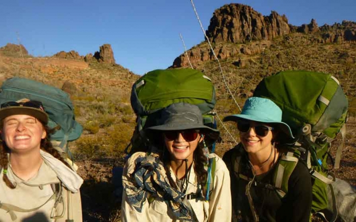 a group of gap year students carrying backpacks smile at the camera while standing in front of a rock formation in texas